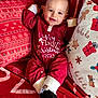 baby, child, smiling, red_clothing, onesie, holiday, christmas, pillow, blanket, patterned_textile, indoors, cute, face, happy, sitting, decor, festive, sock, toddler, celebration