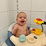 baby, bathtub, bath_time, toy, yellow_flower, blue_seat, white_tiles, water_droplets, smiling, happy, child, infant, bathroom, playful, sitting, cute, naked_upper_body, fun, indoor, person
