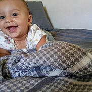 Jordan joined the competition — help win amazing prizes! baby, smiling, happy, face, curly_hair, blanket, bed, pillow, indoor, child, cute, infant, person, clothing, pattern, texture, toddler, home, portrait, cozy
