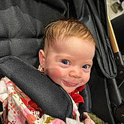 Hazel is registered to the contest to win money with this photo: baby, child, stroller, smile, face, earring, clothing, floral_pattern, hand, cute, infant, person, portrait, happy, young_child, fabric, closeup, indoor, seat, head