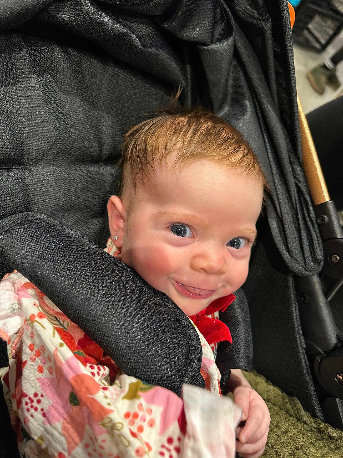 Hazel is registered to the contest to win money with this photo: baby, child, stroller, smile, face, earring, clothing, floral_pattern, hand, cute, infant, person, portrait, happy, young_child, fabric, closeup, indoor, seat, head