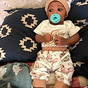 Lacina is registered to the contest to win money with this photo: baby, pacifier, cushion, patterned_clothing, hat, infant, blanket, socks, cute, indoor, person, child, fabric, animal_print, comfort, resting, soft_toys, home, portrait, relax