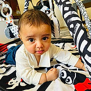 Arham is registered to the contest to win money with this photo: baby, child, infant, playmat, black_and_white, toy, curious, indoor, floor, clothing, face, person, cute, young, lying_down, pattern, decor, toddler, expression, eyes