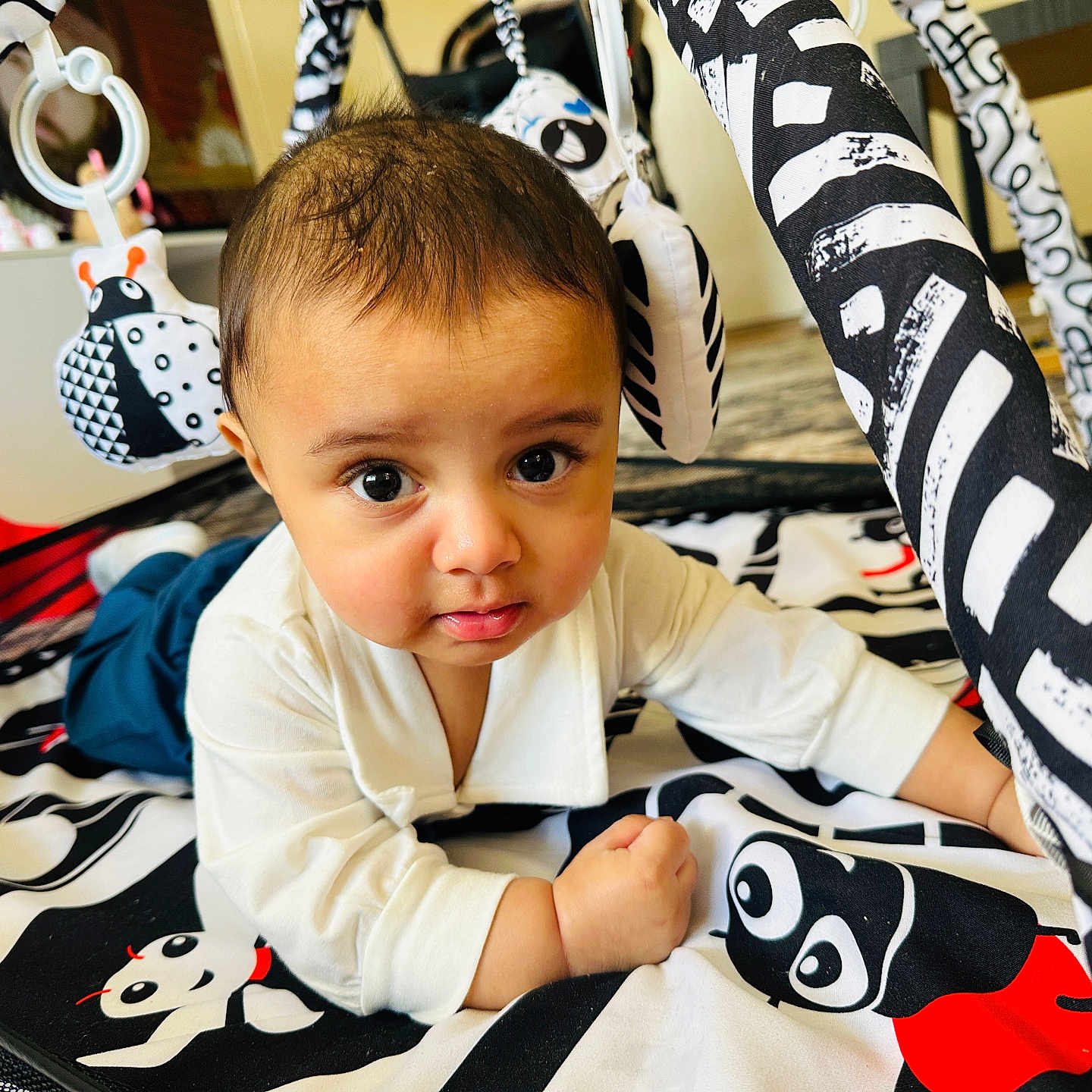 Arham is registered to the contest to win money with this photo: baby, black_and_white, child, clothing, curious, cute, decor, expression, eyes, face, floor, indoor, infant, lying_down, pattern, person, playmat, toddler, toy, young