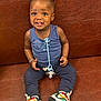 Aboubakar Khalil a rejoint le concours — aidez-le/la à gagner de superbes lots ! toddler, child, smiling, sitting, indoors, leather_couch, tank_top, pacifier, colorful_sneakers, hair_bantu_knots, happy, cute, portrait, young_child, skin, clothing, footwear, person, baby_accessory, casual