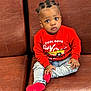 toddler, child, boy, red_sweater, jeans, red_socks, brown_leather_couch, sitting, indoor, curious_expression, portrait, hairstyle, bantu_knots, casual_clothing, young_child, cute, fashion, hands, feet, person