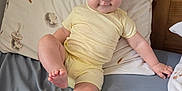 Lilianna is registered to the contest to win money with this photo: baby, child, bed, pillow, yellow_clothing, smile, face, leg, foot, hand, wooden_headboard, bedroom, cute, infant, playful, indoors, person, rest, cozy, pajamas