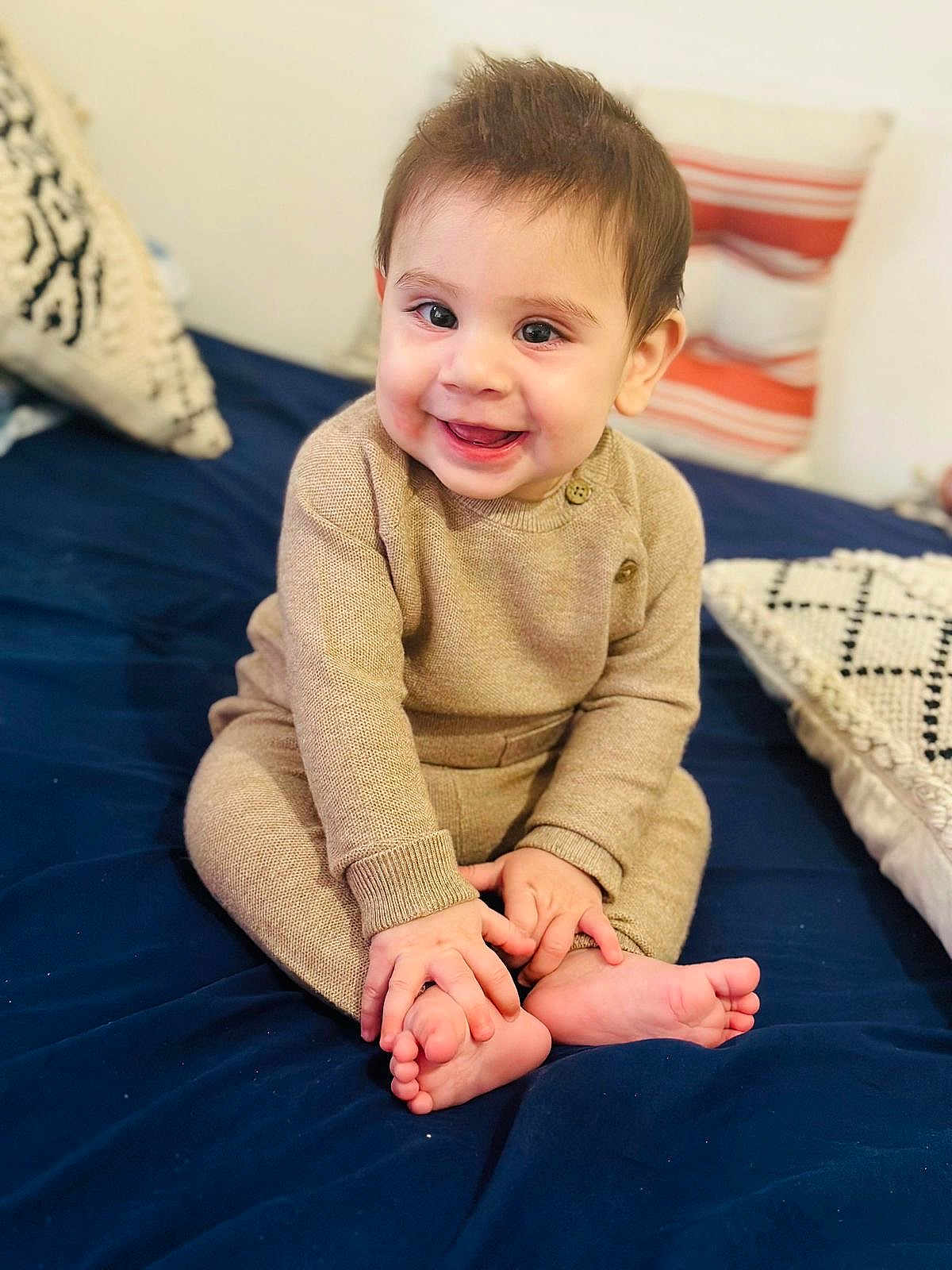 Muhammad is registered to the contest to win money with this photo: baby, child, smiling, sitting, indoors, bed, pillow, knitwear, cozy, happy, cute, portrait, infant, person, feet, hands, home, soft, casual, warm