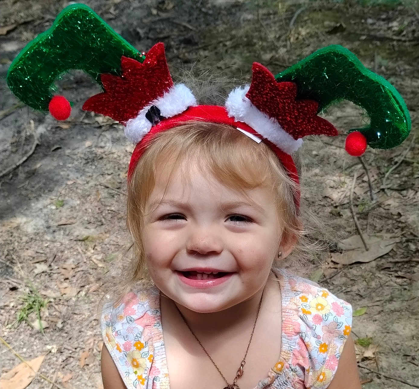 Victoria is registered to the contest to win money with this photo: child, toddler, smiling, face, headband, elf_ears, outdoor, nature, dirt, leaves, flower_print, dress, necklace, happy, young_child, holiday, festive, cute, portrait, daylight