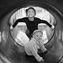 baby, black_and_white, candid, child, clothing, expression, fun, happy, headband, jacket, joy, outdoor, person, playground, playing, portrait, slide, smiling, toddler, tunnel