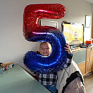 Tiago a rejoint le concours — aidez-le/la à gagner de superbes lots ! child, balloon, number_5, smiling, indoor, living_room, television, cartoon, table, glass_table, jacket, spiderman, boy, happy, clothing, chair, celebration, birthday, person, home