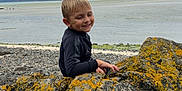 Tiago a rejoint le concours — aidez-le/la à gagner de superbes lots ! child, boy, smiling, rocks, lichen, coast, seaside, cloudy_sky, outdoor, nature, water, shore, landscape, casual_clothing, happy, playful, daylight, scenic, youth, relaxing