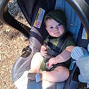Michael joined the competition — help win amazing prizes! baby, child, car_seat, outdoor, sunlight, blue_eyes, hooded_clothing, socks, wood_chips, seatbelt, infant, cute, smiling, person, closeup, portrait, playground, shade, fabric, toy