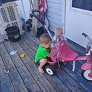 Sky joined the competition — help win amazing prizes! toddler, child, tricycle, porch, wooden_floor, toy, outdoor, barefoot, american_flag, door, plastic_tricycle, clothing, play, curious, sitting, baby, handle, wheel, house, daylight