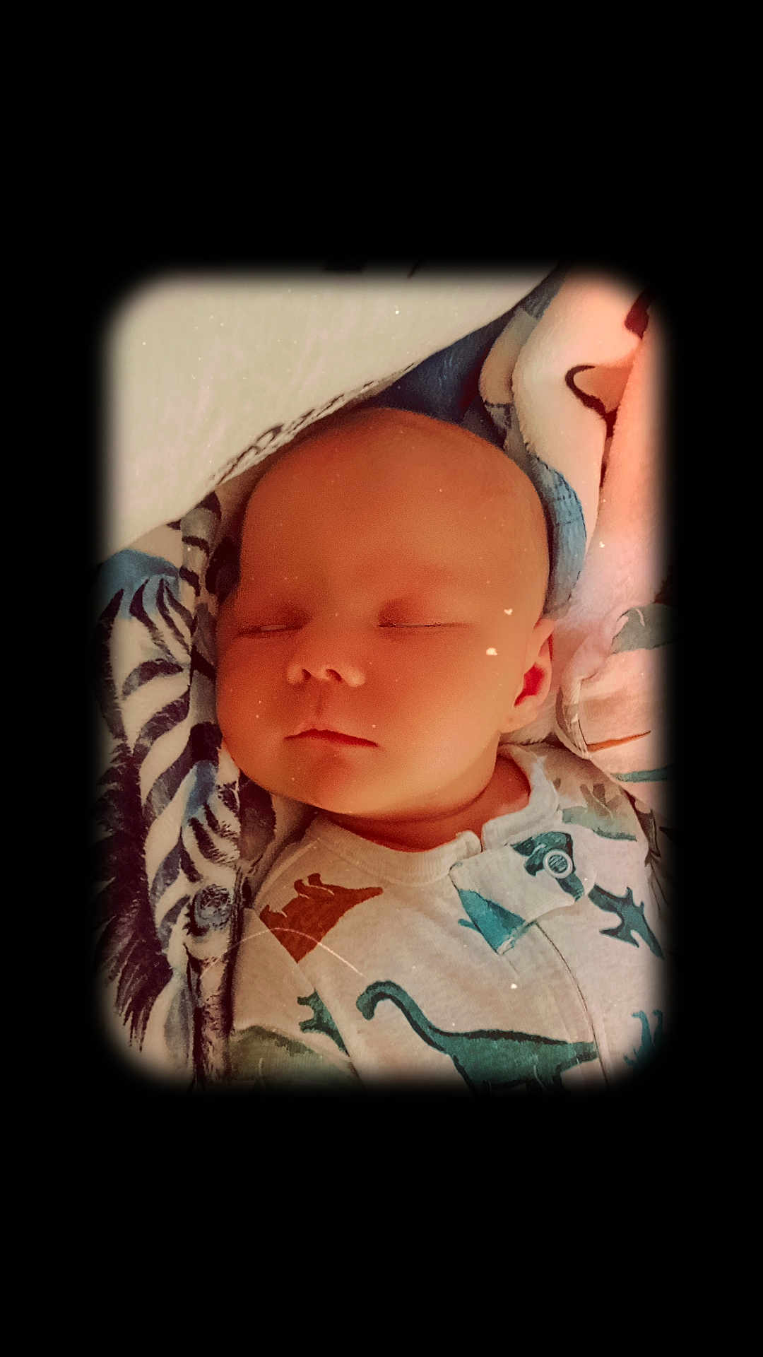 Lucas is registered to the contest to win money with this photo: baby, sleeping, infant, blanket, pajamas, dinosaur_pattern, cute, peaceful, face, child, portrait, resting, soft_light, indoors, young, cozy, closeup, head, skin, comfort