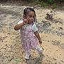child, girl, peace_sign, pink_dress, braided_hair, beads, outdoor, ground, sand, greenery, playful, pose, white_shirt, shoes, fashion, young, nature, casual, daytime, person