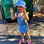 Bloom joined the competition — help win amazing prizes! child, girl, smiling, peace_sign, bucket_hat, denim_dress, orange_shirt, pink_shoes, outdoor, pavement, sunlight, shopping_cart, dumpster, fence, beads, happy, fashion, casual, playful, portrait