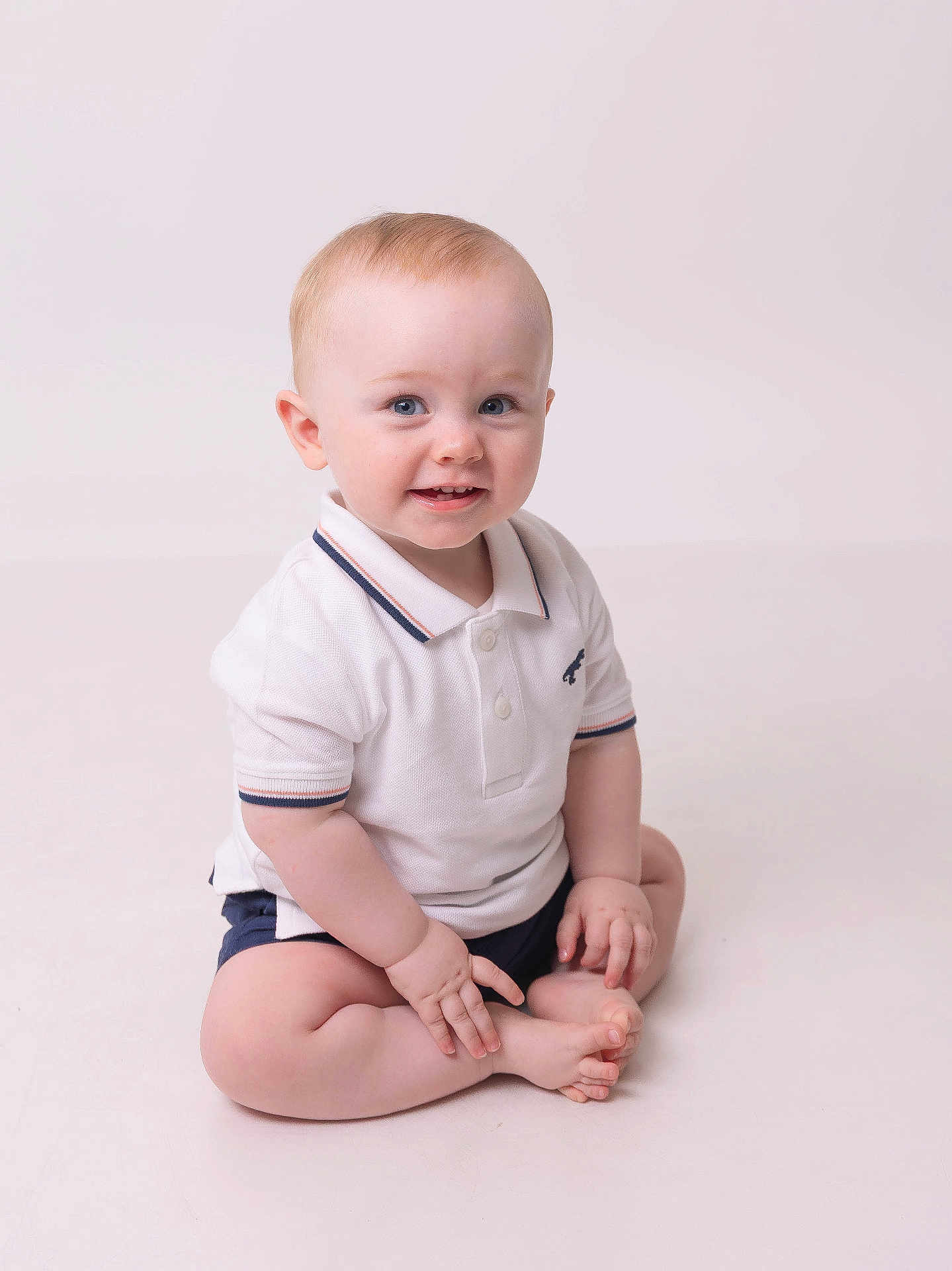 Joshua joined the competition — help win amazing prizes! baby, child, infant, smiling, sitting, white_polo, shorts, blue_eyes, cute, portrait, studio, light_background, hands, feet, happy, toddler, skin, face, young, indoors