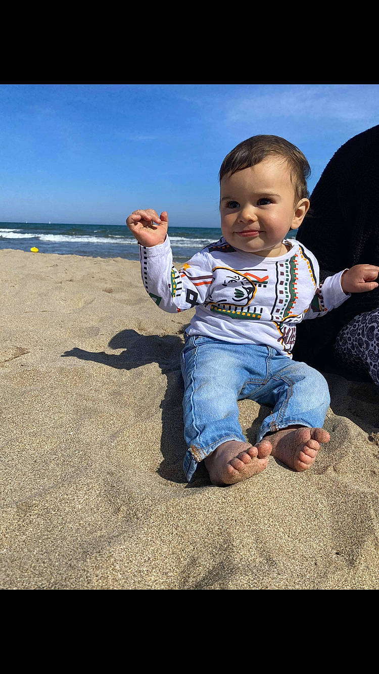Ilyas participe au concours pour gagner de l'argent avec cette photo : azure, baby, baby_toddler_clothing, beach, finger, flash_photography, fun, gesture, grass, happy, joy, people_in_nature, person, sitting, sky, sleeve, smile, standing, sunlight, toddler