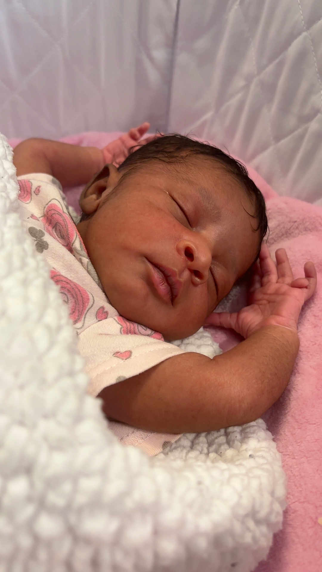 Naomi is registered to the contest to win money with this photo: newborn, baby, sleeping, blanket, onesie, floral_pattern, pink, white, soft, cozy, infant, peaceful, portrait, cute, face, hand, skin, rest, bed, quilted