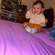 Jeremiah is registered to the contest to win money with this photo: toddler, child, smiling, bed, purple_bedspread, socks, long_sleeve_shirt, pants, furniture, dresser, plastic_drawers, star_wall_decor, indoors, happy, person, room, cozy, casual, cute, portrait