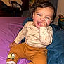 baby, child, smiling, sitting, bed, blanket, clothing, face, indoor, person, pants, shirt, toy, happy, cute, sock, hair, room, furniture, expression