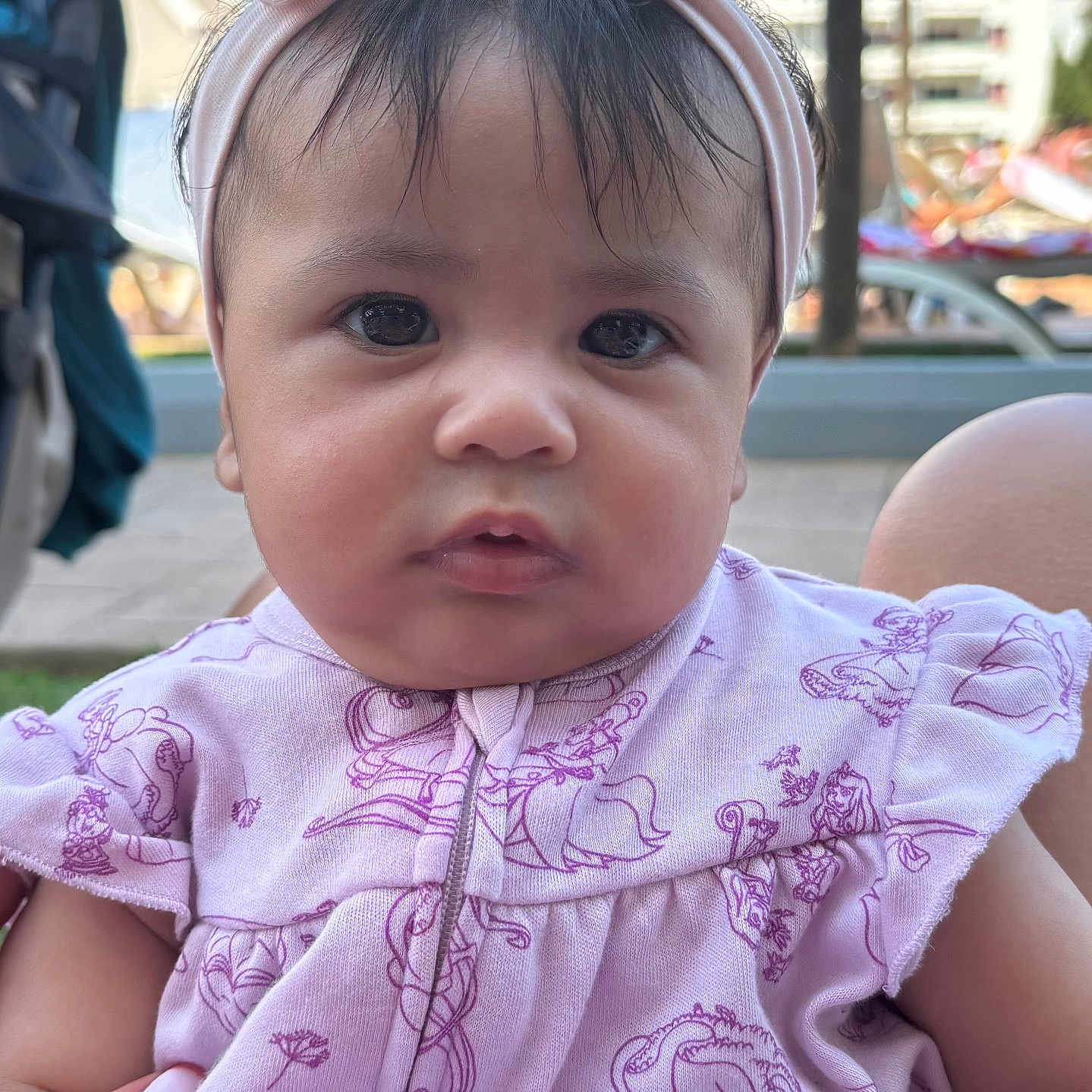 Aida a rejoint le concours — aidez-le/la à gagner de superbes lots ! baby, background, child, close_up, curious, cute, daylight, expression, eyes, face, hand, headband, infant, outdoor, person, pink_clothing, portrait, sitting, skin, young