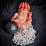 baby, newborn, sleeping, knitted_hat, basketball, basketball_net, black_background, infant, cute, sports, orange_hat, white_net, hand, foot, portrait, cozy, child, soft_texture, resting, indoor