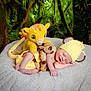 baby, newborn, sleeping, plush_toy, stuffed_animal, yellow_hat, knit_hat, forest_background, blanket, cozy, child, cute, smiling, infant, nature, greenery, soft_texture, peaceful, resting, animal_toy