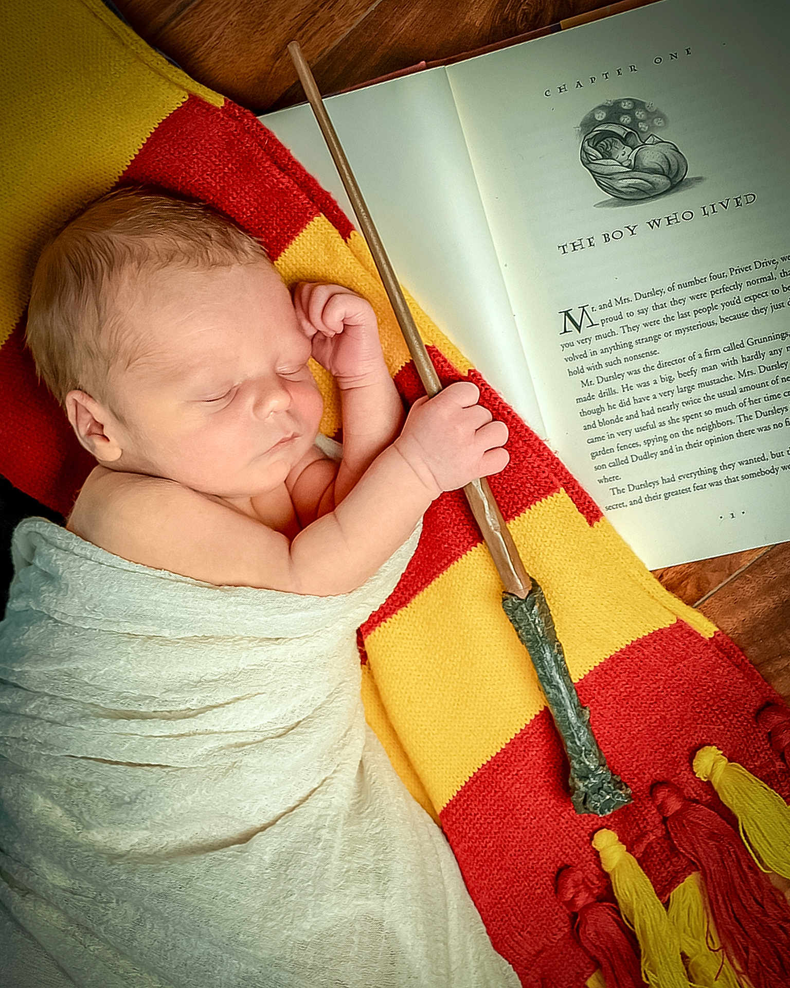 Charlie joined the competition — help win amazing prizes! baby, newborn, sleeping, blanket, scarf, red, yellow, wizard_wand, book, open_book, text, wood_floor, hand, face, portrait, cozy, magic, child, indoor, peaceful