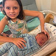 Lilly joined the competition — help win amazing prizes! child, newborn, baby, hospital, bassinet, sibling, family, smile, sleeping, clothing, person, indoor, bed, blanket, adult, glasses, happy, care, love, tender