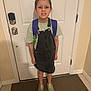 Lilly is registered to the contest to win money with this photo: child, indoor, door, backpack, dress, shirt, sneakers, floor, carpet, wall, young, person, standing, smile, hair, necklace, clothing, footwear, casual, home