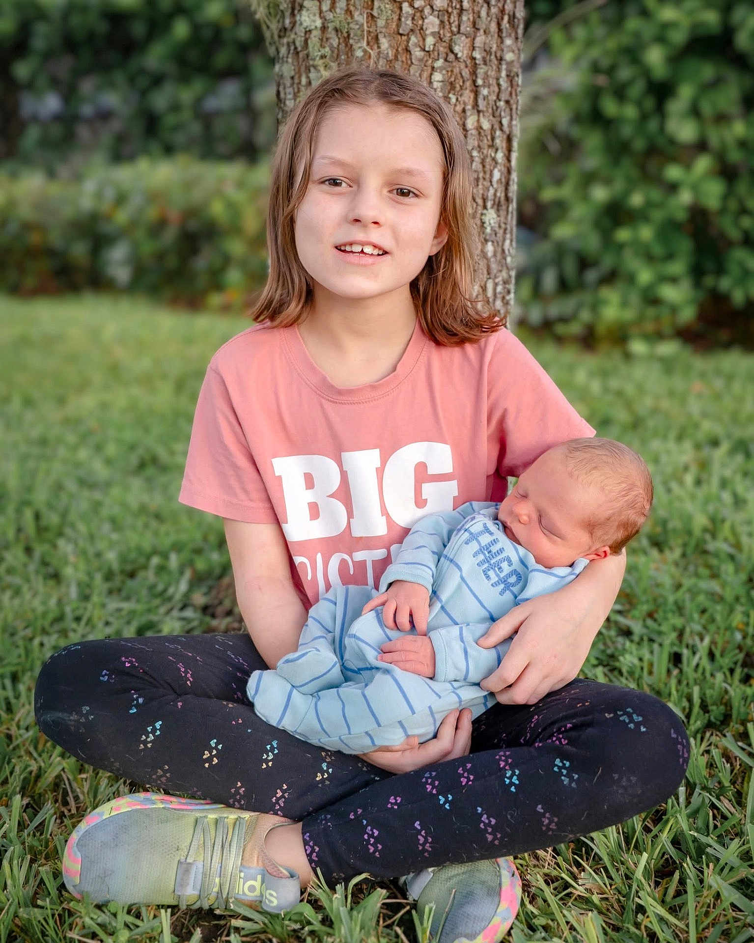 Lilly is registered to the contest to win money with this photo: child, baby, big_sister, newborn, grass, tree, outdoor, nature, sitting, smiling, holding, family, portrait, cute, clothing, footwear, person, young, toddler, peaceful