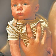 Myles joined the competition — help win amazing prizes! baby, child, hand, person, face, blue_eyes, striped_clothing, ring, wristband, holding, portrait, indoor, skin, expression, infant, young_child, closeup, human, adult_hand, warm_lighting