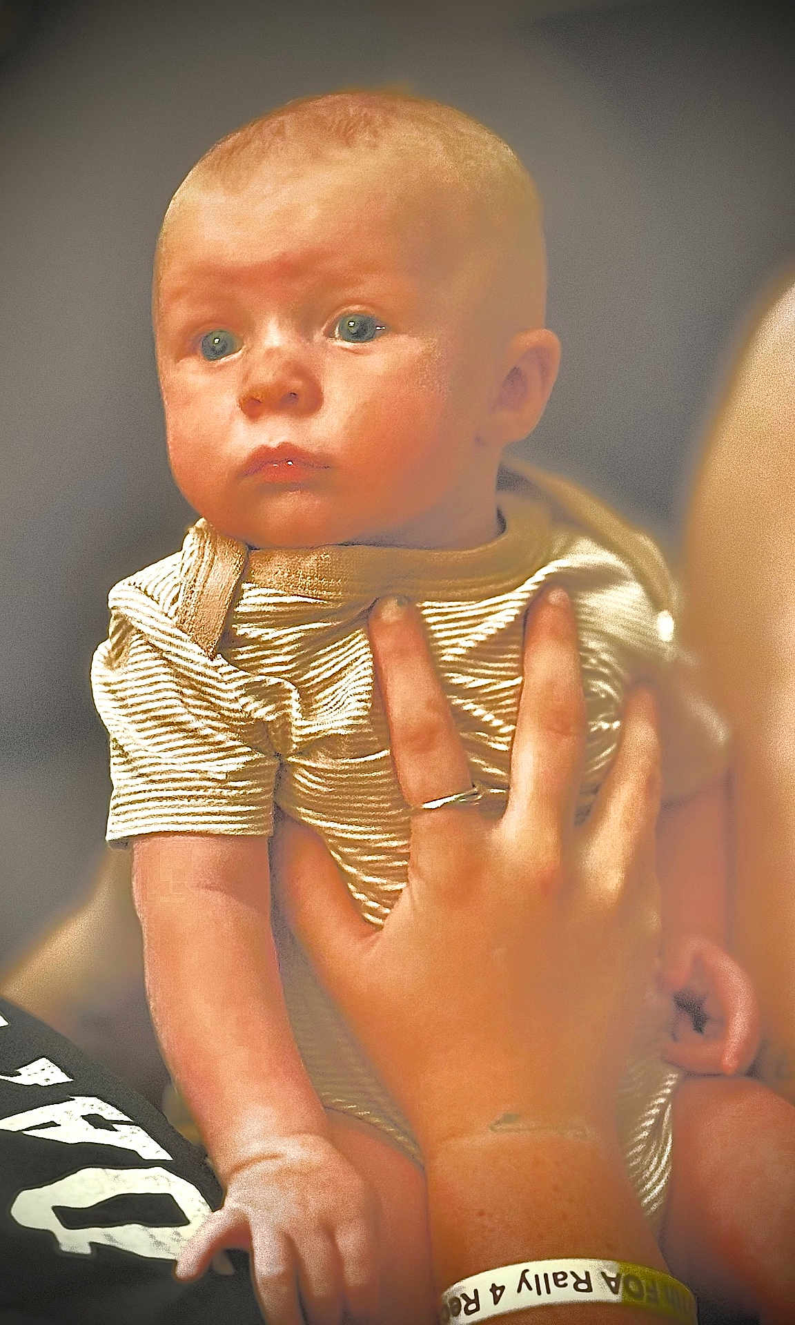 Myles joined the competition — help win amazing prizes! baby, child, hand, person, face, blue_eyes, striped_clothing, ring, wristband, holding, portrait, indoor, skin, expression, infant, young_child, closeup, human, adult_hand, warm_lighting