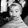 baby, child, headband, bow, face, smile, portrait, black_and_white, close_up, cute, infant, person, soft, pillow, indoors, eyes, expression, young, happy, head