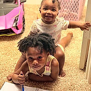 Nalani joined the competition — help win amazing prizes! child, baby, notebook, pen, carpet, toy_car, indoor, drawing, smiling, happy, play, baby_clothes, toddler, person, hair, floor, room, door, basket, cute