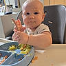 baby, child, cute, eating, food, high_chair, home, indoor, infant, kitchen, mashed_food, mealtime, messy, plate, portrait, sitting, smiling, spoon, tray, vegetables