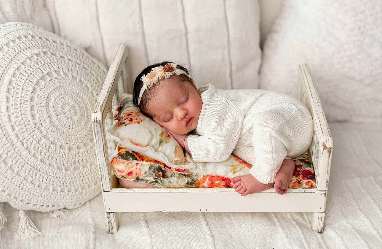 Brielle joined the competition — help win amazing prizes! baby, blanket, child, cozy, cute, floral_cushion, flower_headband, headband, indoors, infant, newborn, peaceful, pillow, portrait, resting, sleeping, small_bed, soft_texture, white_outfit, wooden_bed