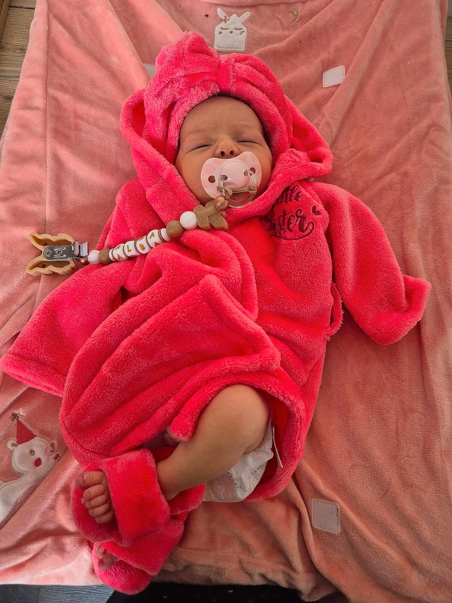 Alba participe au concours pour gagner de l'argent avec cette photo : baby, newborn, infant, pacifier, pacifier_clip, pink_robe, hood, blanket, plush_blanket, diaper, bare_foot, sleepy, beads, clip, soft_texture, cozy, lying_down, wooden_floor, cute, person