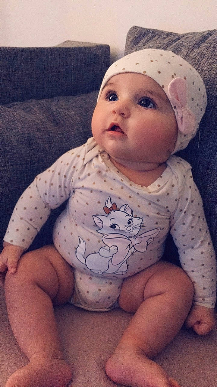 Zaïna a rejoint le concours — aidez-le/la à gagner de superbes lots ! baby, baby_toddler_clothing, beanie, cap, cheek, child, eye, face, head, headgear, headwear, lip, person, pink, sitting, skin, sleeve, toddler