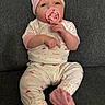 baby, pacifier, pajamas, infant, child, sitting, couch, fabric, clothing, hand, footwear, headwear, face, pink, white, pattern, indoor, cute, portrait, cozy
