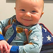 Silas is registered to the contest to win money with this photo: baby, child, smiling, onesie, infant, hand, indoor, person, face, blue_clothing, patterned_clothing, striped_pants, framed_picture, flag, american_flag, patriotic, wall, adult_hand, holding, portrait