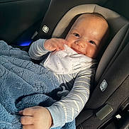 Armaan joined the competition — help win amazing prizes! baby, infant, child, smiling, car_seat, vehicle, blanket, bib, striped_clothing, sleeves, portrait, indoors, travel, safety_harness, cozy, happy, face, hands, sunlight, photograph