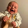 baby, smile, happy, infant, child, hand, finger, white_clothing, bear_patch, holding, portrait, cute, playful, human, skin, face, joy, expression, indoor, cozy