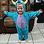 arms_outstretched, barefoot, blue, child, clothing, costume, couch, cute, face, furniture, hood, indoor, living_room, monster, person, smile, tile_floor, toddler, toy, yellow_horns