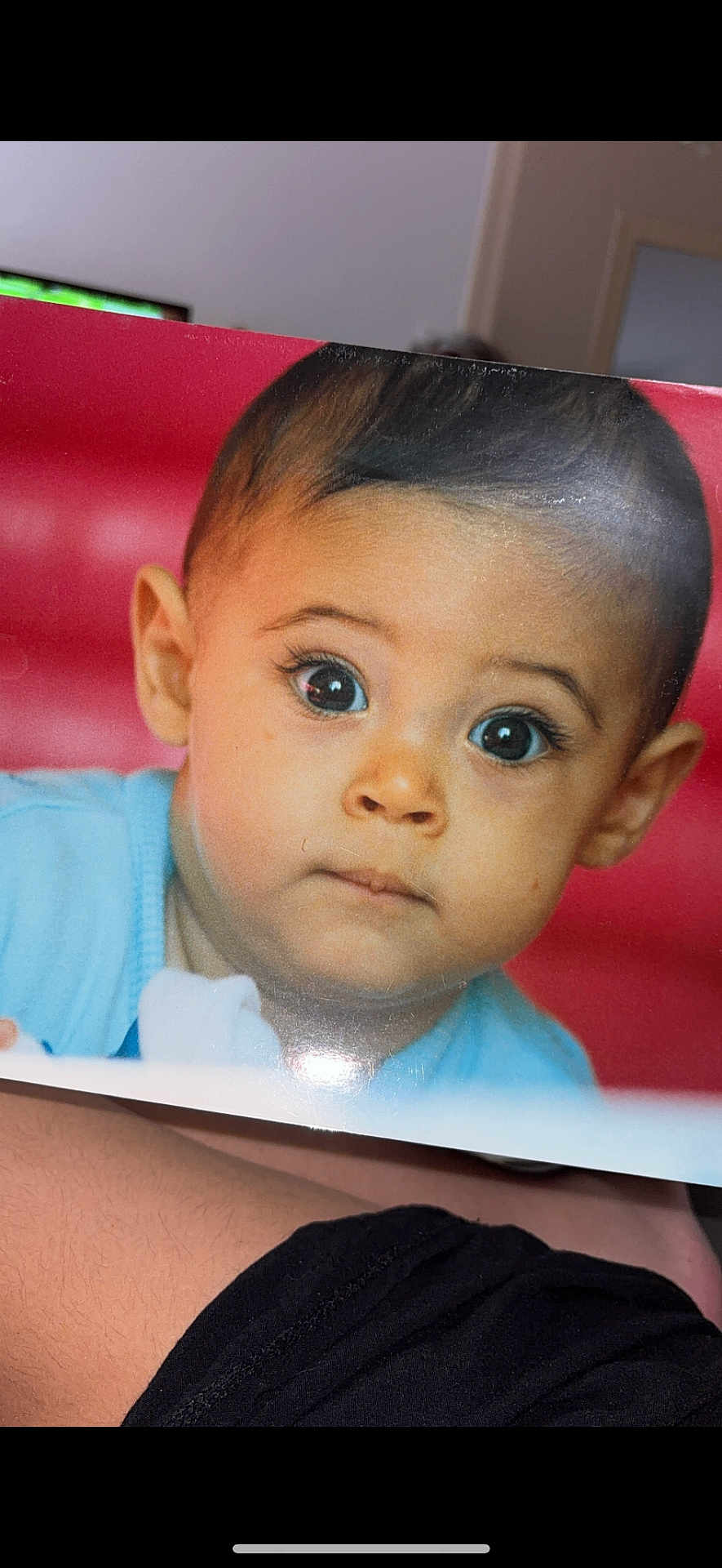 Isleym a rejoint le concours — aidez-le/la à gagner de superbes lots ! baby, child, face, eyes, portrait, expression, curious, blue_clothing, closeup, skin, head, person, photograph, arm, black_clothing, red_background, print, holding, indoor, young_child