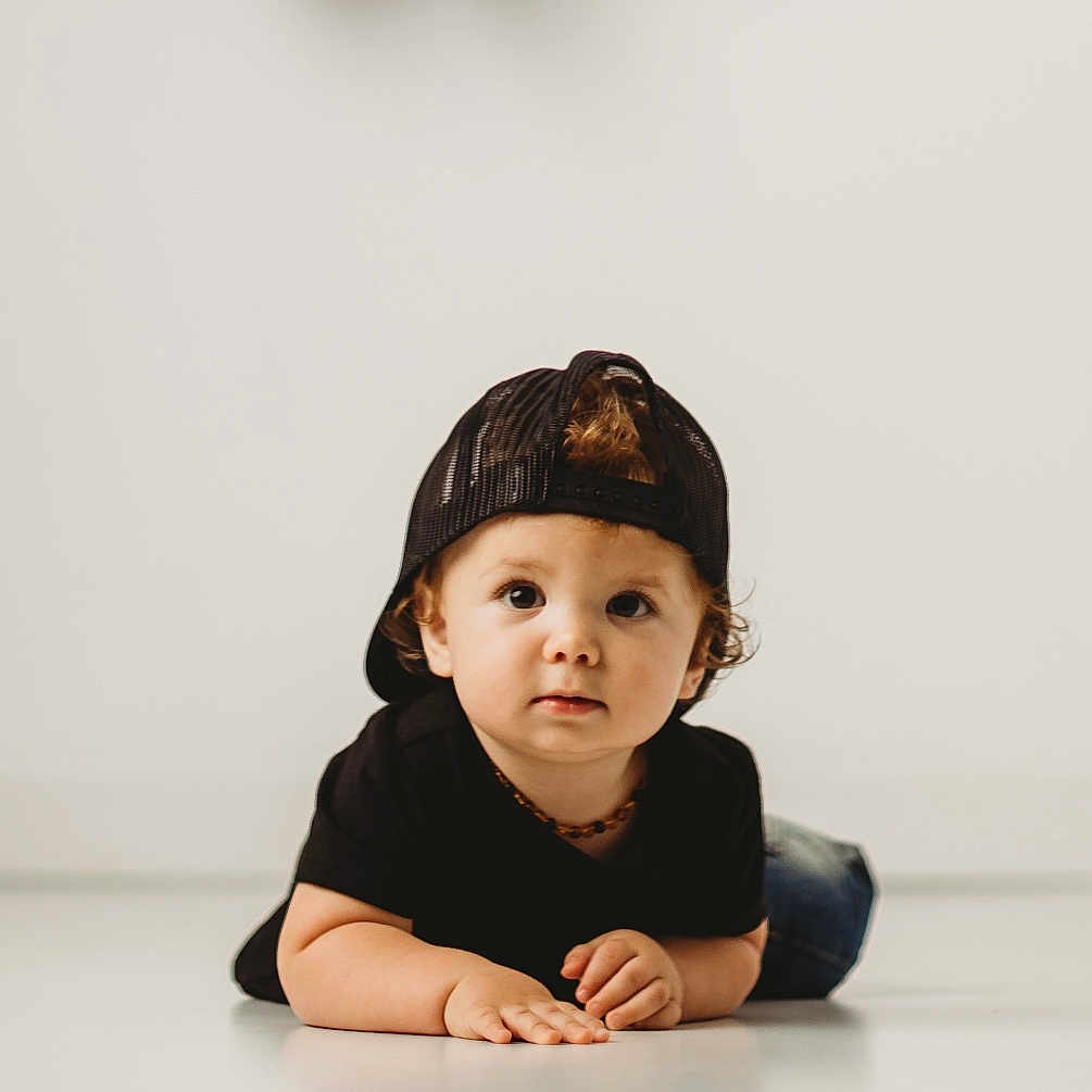 Jenson joined the competition — help win amazing prizes! child, toddler, baby, portrait, studio, floor, lying_down, backwards_cap, black_clothing, casual, curly_hair, brown_hair, face, eyes, hands, crawling, fashion, indoor, minimalist, photography