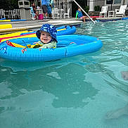 Jackson is registered to the contest to win money with this photo: baby, child, swimming_pool, inflatable_ring, water, hat, blue, smile, outdoor, poolside, people, umbrella, summer, fun, recreation, floating, sitting, play, vacation, leisure