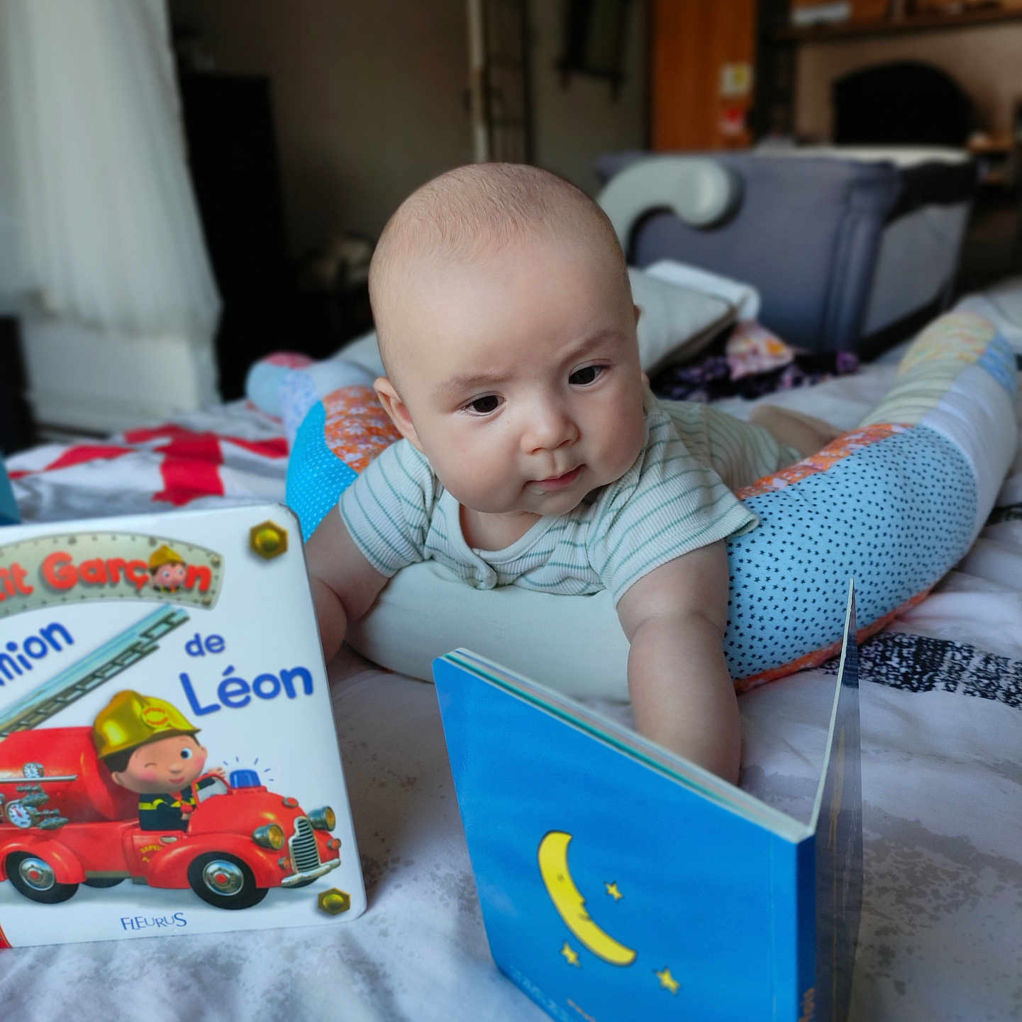 Raphaël a rejoint le concours — aidez-le/la à gagner de superbes lots ! baby, bed, blanket, book, child, colorful, cozy, curious, early_learning, education, floor, furniture, indoor, infant, person, playtime, reading, soft_light, striped_clothing, toy
